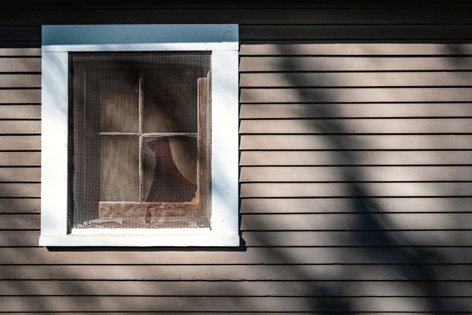 A boarded window set in dark horizontal clapboard siding.