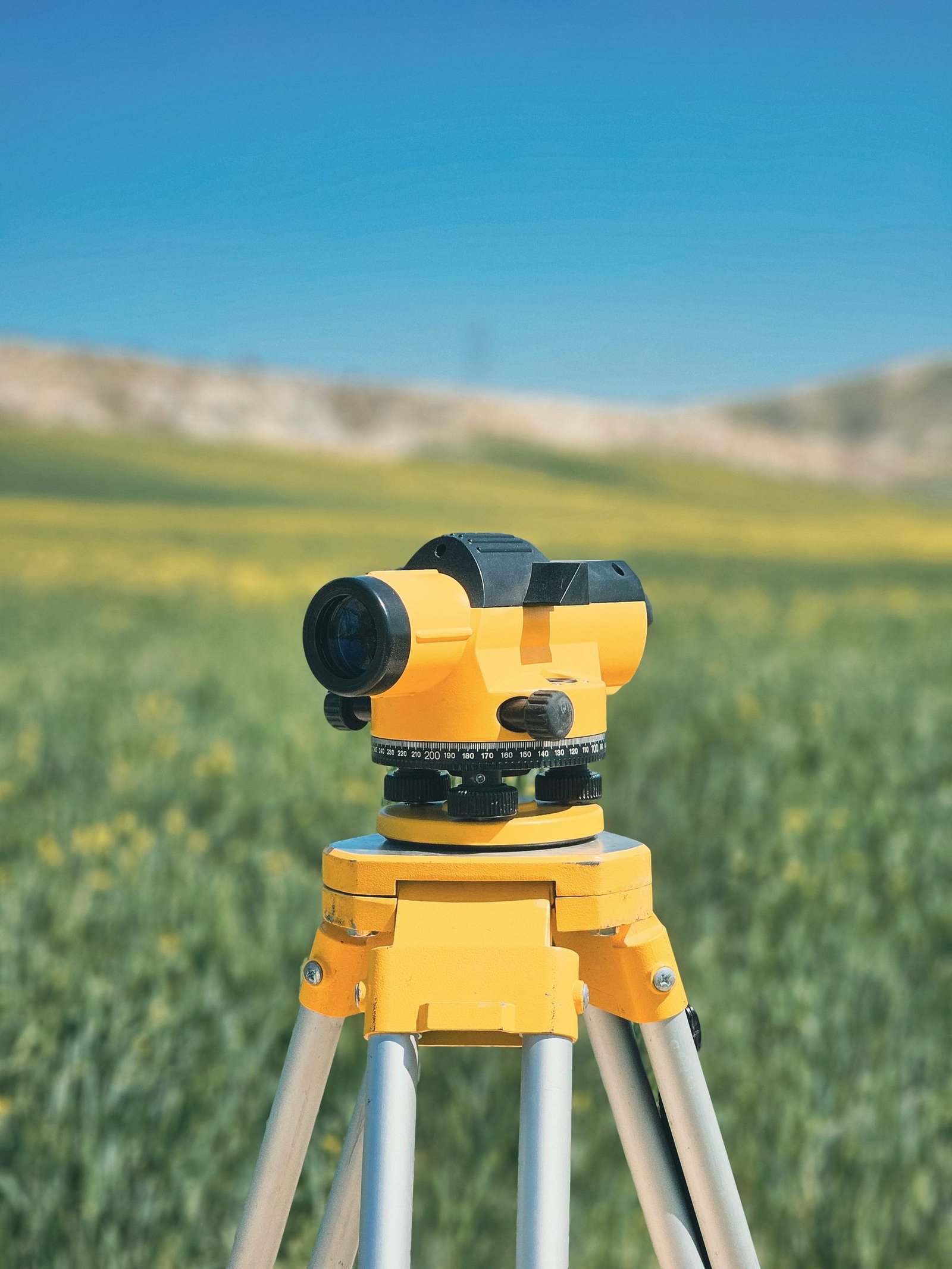 A surveyor's optical level set up on a tripod in a field.